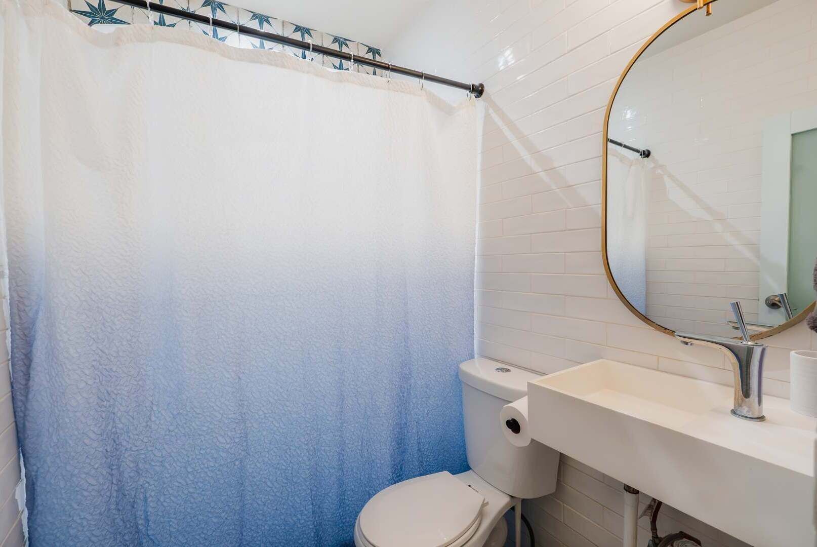 Une salle de bain avec des toilettes blanches, un lavabo blanc doté d’un robinet chromé et un rideau de douche bleu.
