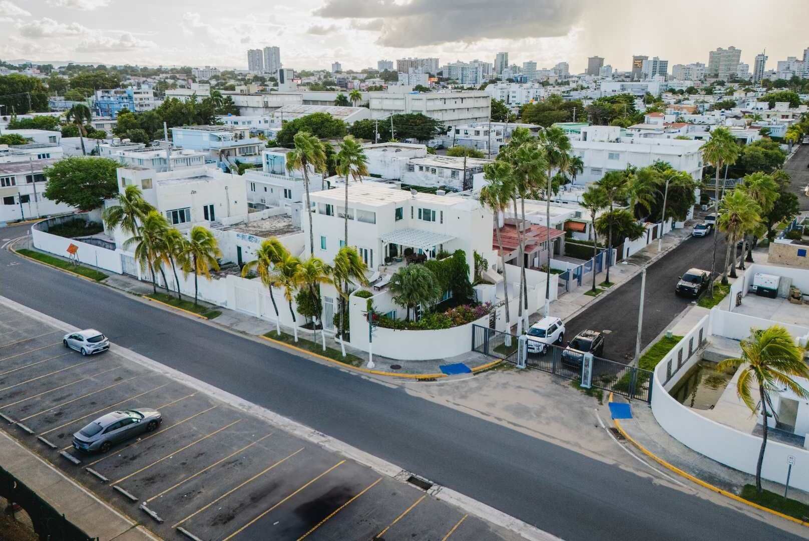 Un quartiere residenziale con edifici bianchi, palme e una strada con auto parcheggiate.