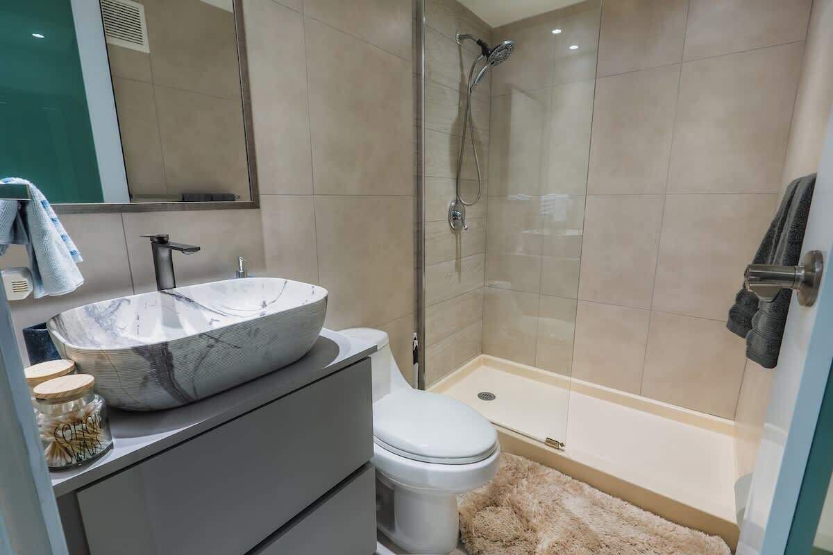 Une salle de bain moderne avec un grand lavabo en marbre, des toilettes, une douche en verre et un sol carrelé de couleur beige.