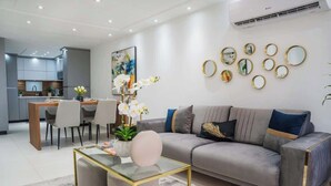 A modern living room with a grey sofa, a glass coffee table, and a dining area with chairs and a wooden table. - Isla The Sunset Abode in Ocean Club, Rincón (Rincon)
