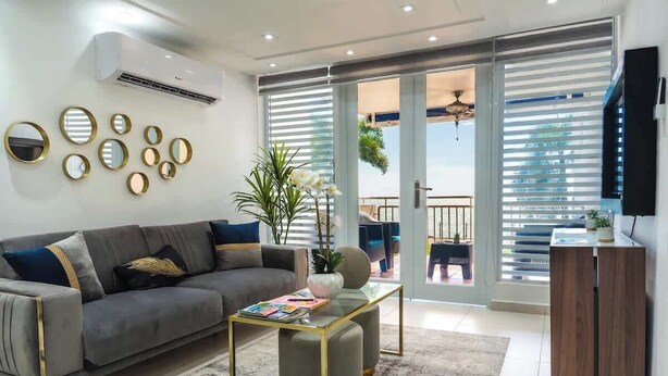 A modern living room with a grey sofa, a glass coffee table, and a wooden cabinet. - Isla The Sunset Abode in Ocean Club, Rincón (Rincon)