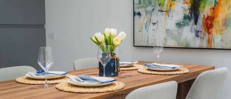 A dining table set with plates, cutlery, and glasses, with a vase of flowers in the center.