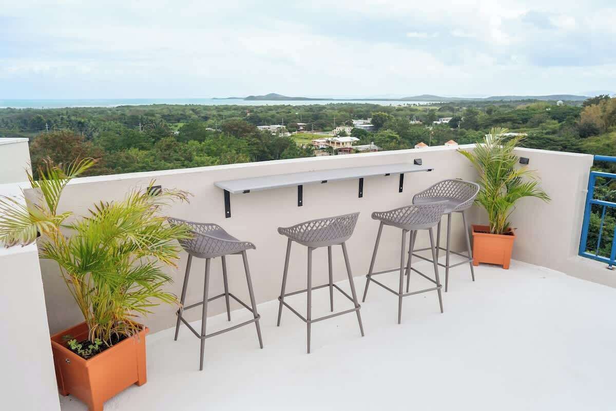 Une terrasse sur le toit avec trois tabourets de bar, une petite étagère et des plantes en pot.