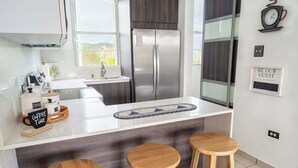 A modern kitchen with a stainless steel refrigerator, a coffee station, and a bar area with stools. - Marbella PH Rooftop Oasis in Costa Brava, Ceiba (Ceiba)