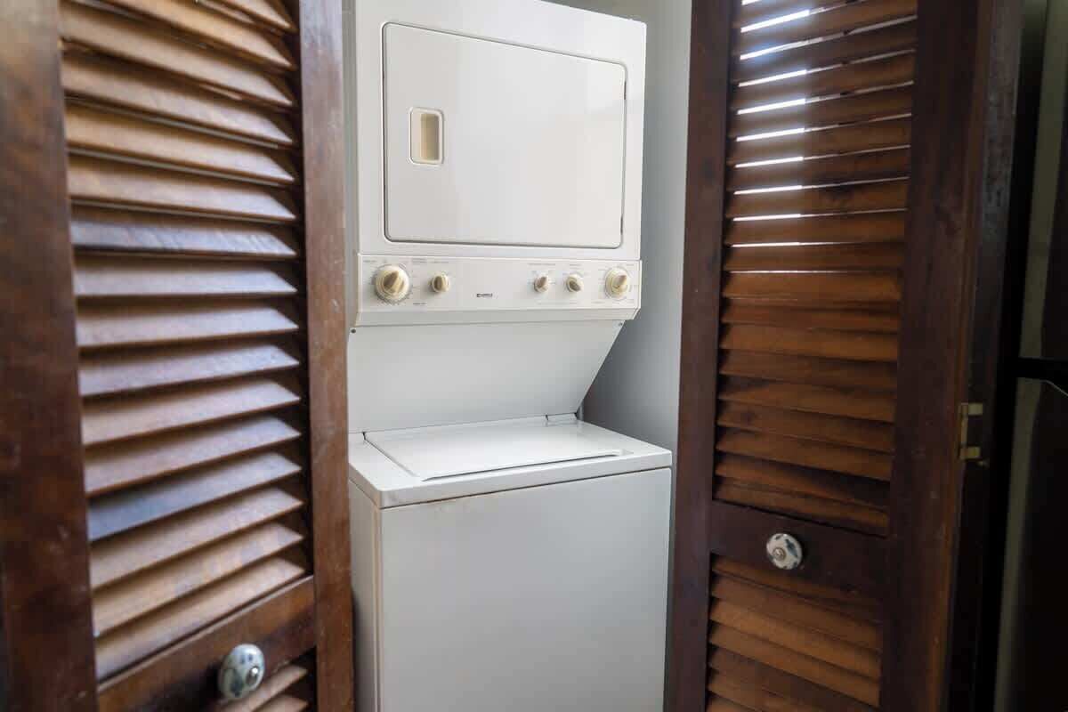 A compact, white laundry room with a built-in washer and dryer, enclosed by wooden slatted doors.