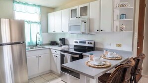 Een moderne keuken met witte kastjes, roestvrijstalen apparatuur en een eethoek met rieten stoelen.