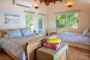 A bedroom with two beds, a wooden headboard, a window with blinds, a painting on the wall, and a ceiling fan. - Le Sirenuse Paradise Haven in Culebra, Island (Culebra)