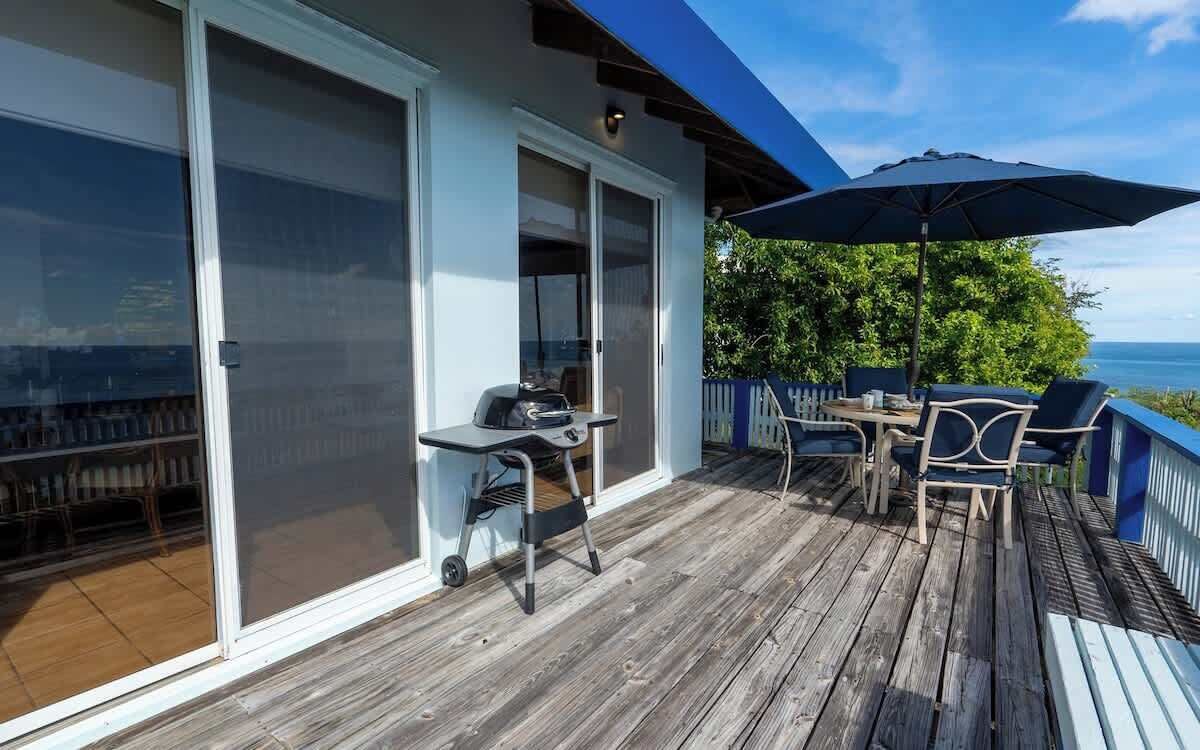 Une terrasse en bois avec un barbecue, du mobilier d’extérieur et une vue sur l’océan.