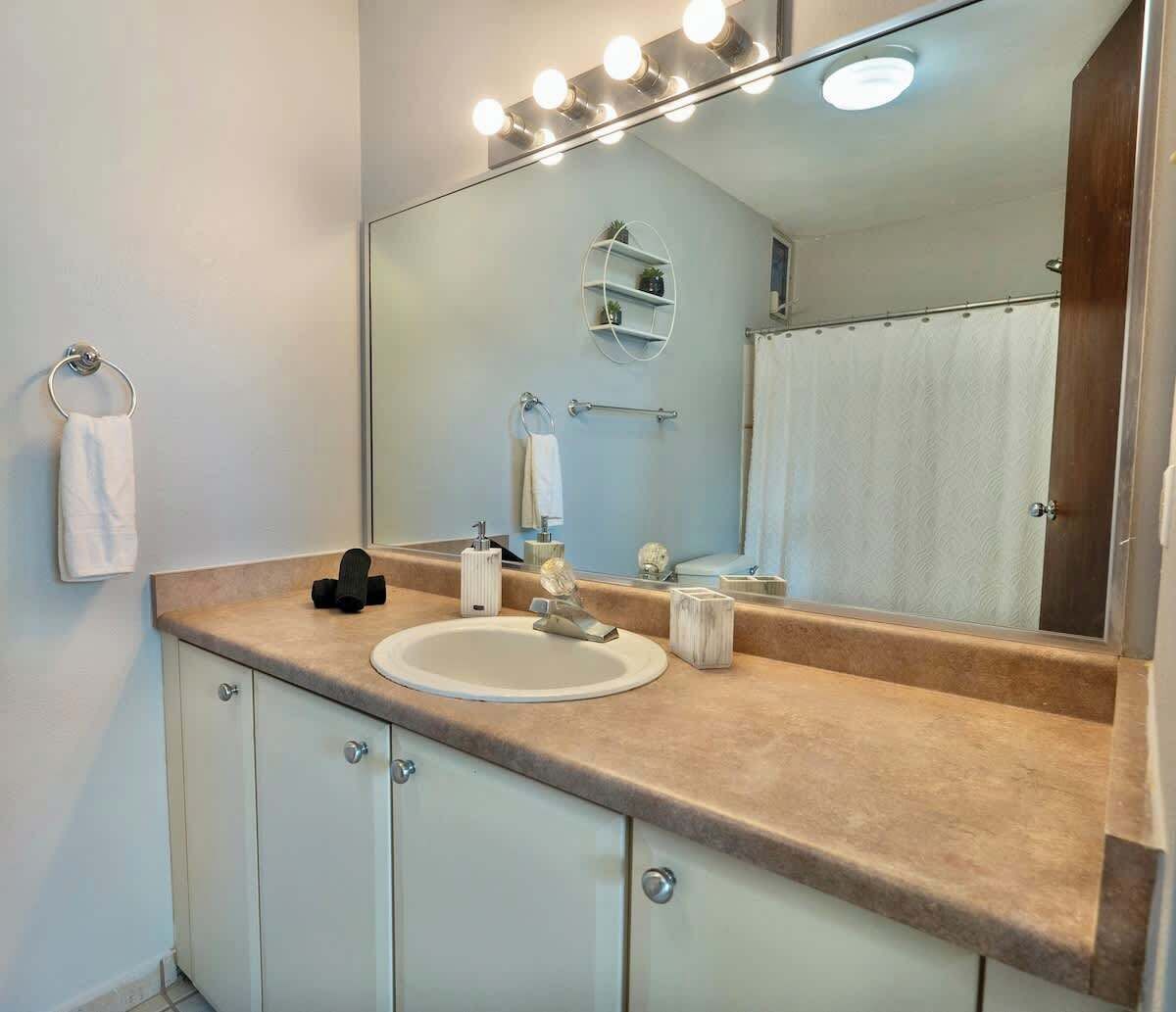 A bathroom with a large mirror, vanity with a sink, and a towel rack.