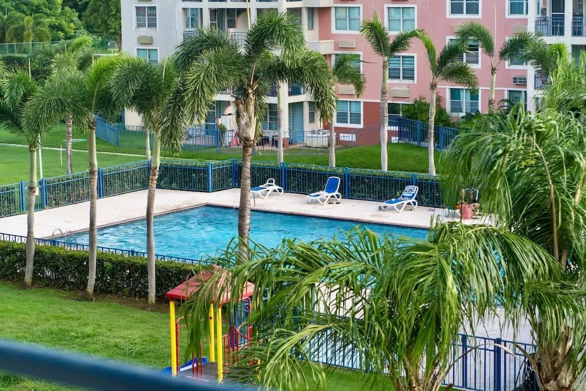 Una piscina rodeada de palmeras y sillas de descanso, con un edificio al fondo.