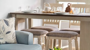 A cozy living room with a blue sofa, wooden dining table, and chairs. A small round table with a plant is in the foreground. - Serenity Beach Vibe Stay in Costa Brava, Ceiba (Ceiba)
