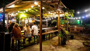 An outdoor dining area with wooden tables and benches, string lights, and potted plants. - Blü Zen, Ideal Couples Stay in Mameyes Rio Grande (Río Grande)