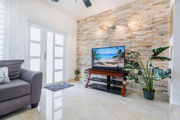A living room with a stone wall, a flat-screen TV, a gray sofa, and potted plants. - Blü Zen, Ideal Couples Stay in Mameyes Rio Grande (Río Grande)