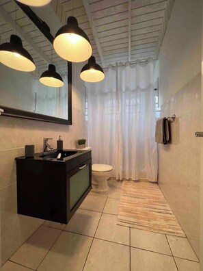 Et moderne badeværelse med en sort kommode, et hvidt toilet og en badeforhæng.