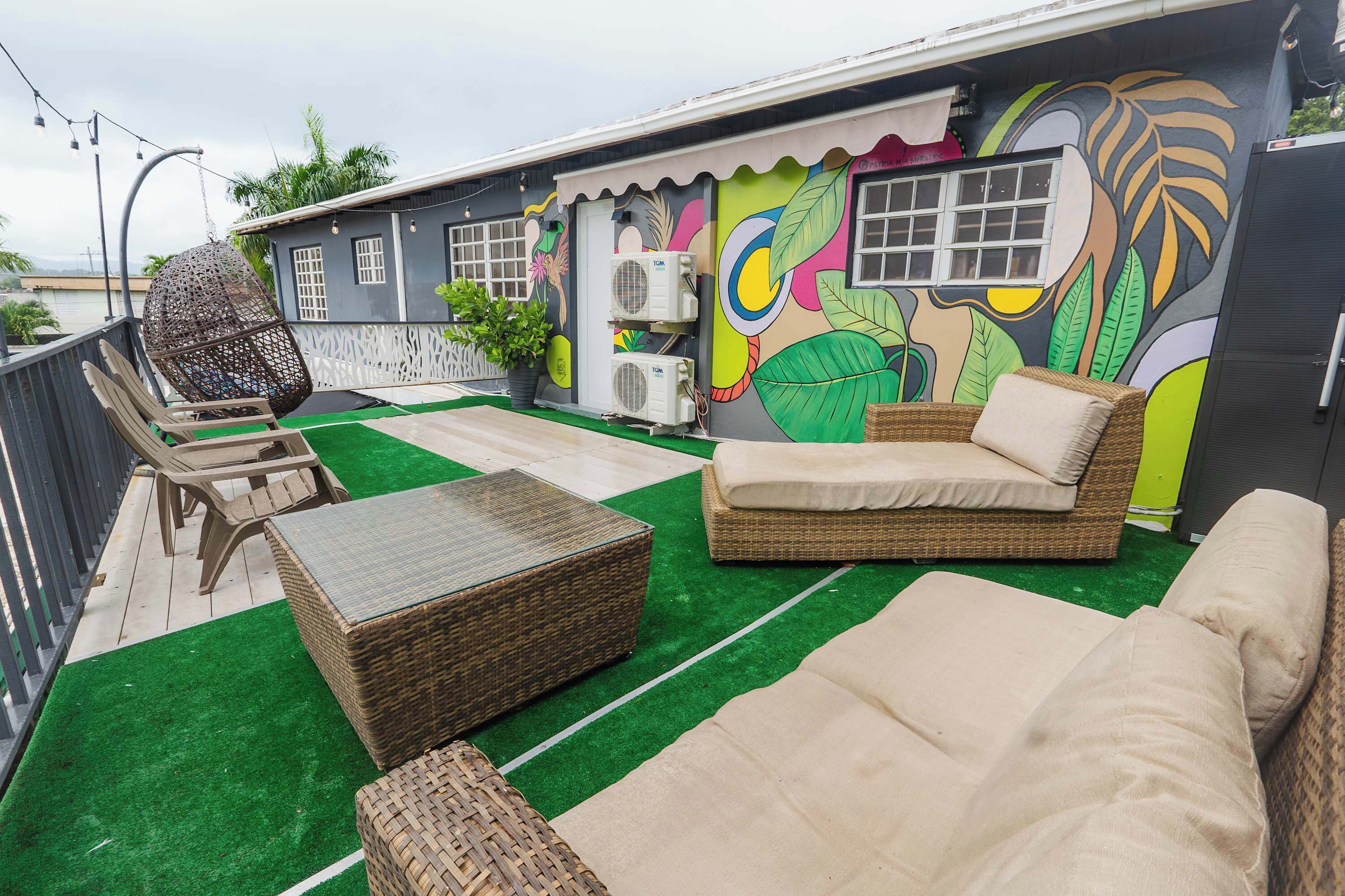A rooftop terrace with wicker furniture, a colorful mural, and air conditioning units.