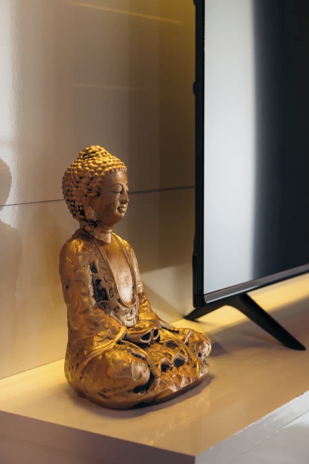 A golden Buddha statue on a white pedestal against a wall.