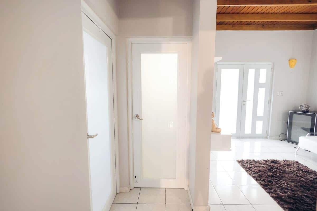 Un pasillo con una puerta blanca, una pared blanca y un piso de baldosas.