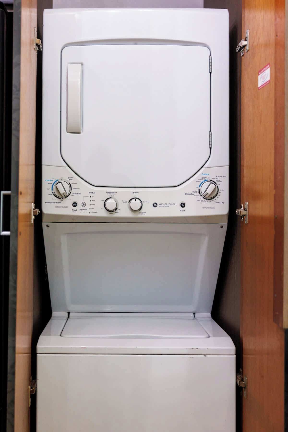 A front view of a white washing machine with control knobs, a start button, and a label indicating it is a permanent press model.