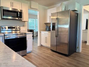 A modern kitchen with stainless steel appliances, white cabinetry, and a wooden floor. - Pool Oasis-Luxe Stay w/ Foosball +Dedicated Desk (Jacksonville)