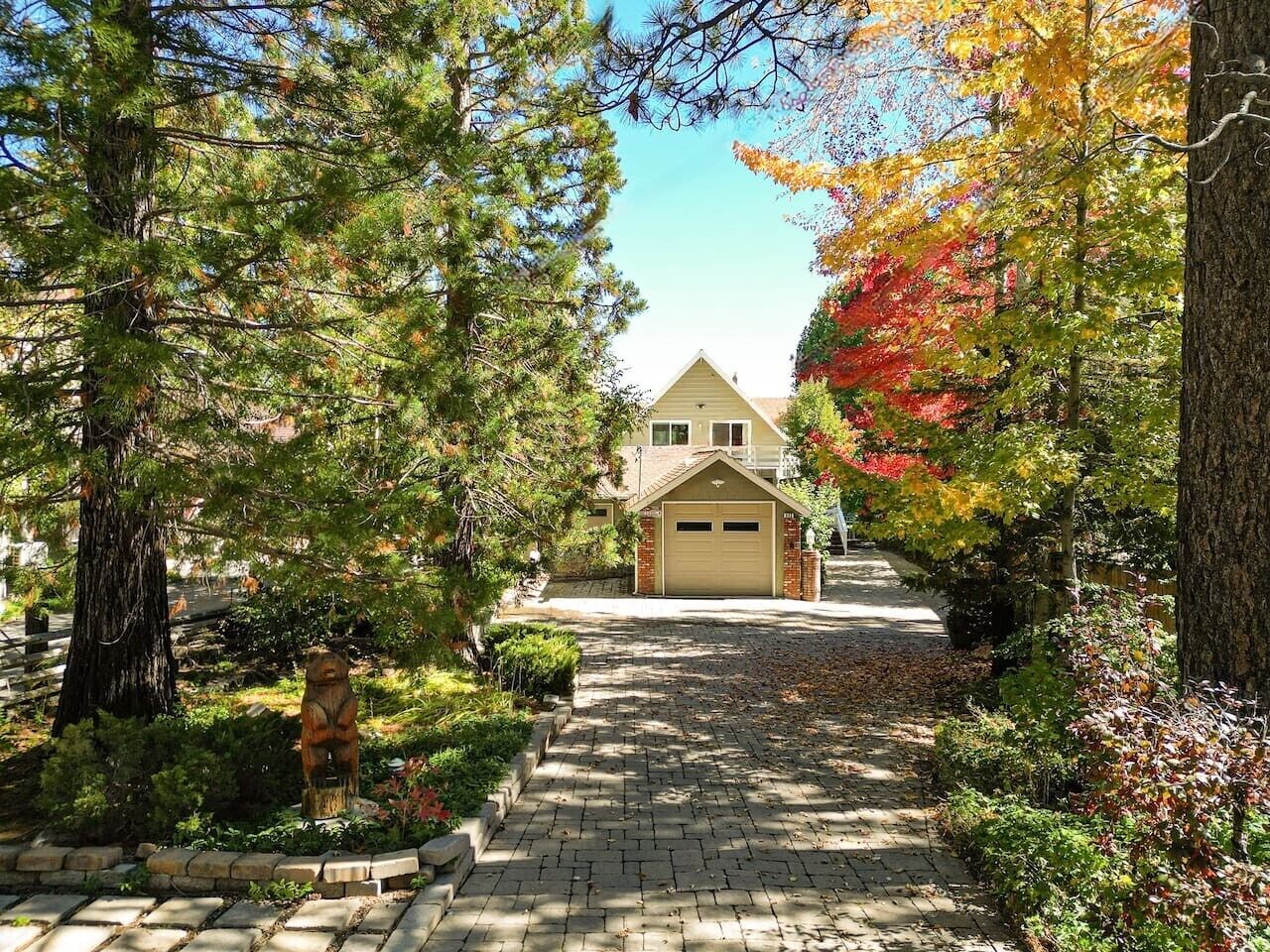 Une allée menant à une maison avec un garage, entourée d’arbres et bordée d’un chemin en pierre.