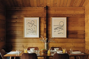 Een houten eetkamer met een tafel voor vier personen, een lijst met kunstwerken aan de muur en een vaas met gedroogde planten.
