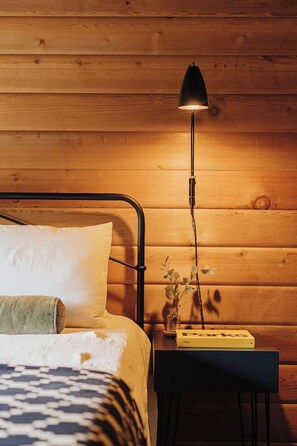 Een bed met een wit kussen en een groen kussen, een zwart metalen frame, een nachtkastje met een lamp en een boek getiteld 'Parks' op het tafeltje.