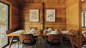 A wooden-paneled dining room with a table set for four, framed artwork on the walls, and a view through the window. - Shadow Wood Lodge, w Hot Tub near Ski Slopes (Big Bear Lake)