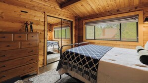 A wooden cabin bedroom with a bed, dresser, and a window with a view of greenery. - Shadow Wood Lodge, w Hot Tub near Ski Slopes (Big Bear Lake)