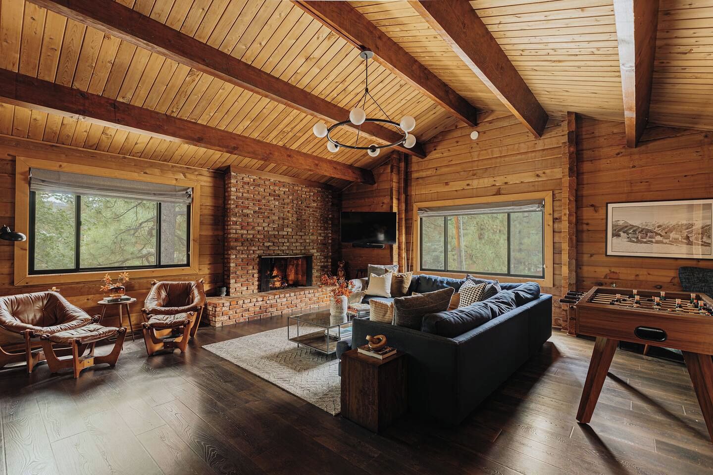 Ein gemütliches Wohnzimmer mit Kamin aus Ziegelsteinen, Ledersesseln, einem dunklen Sofa und einer Holzbalkendecke.