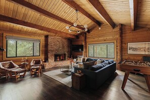 Een gezellige woonkamer met een met baksteen beklede open haard, leren fauteuils, een donkere bank en een houten plafond.
