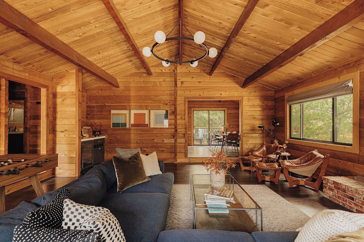 A cozy cabin interior with a wooden ceiling, a sofa set, a coffee table, and a dining area.
