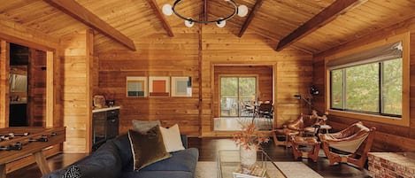 Interior acogedor de una cabaña con techo de madera, un conjunto de sofás, una mesa de centro y una zona de comedor.