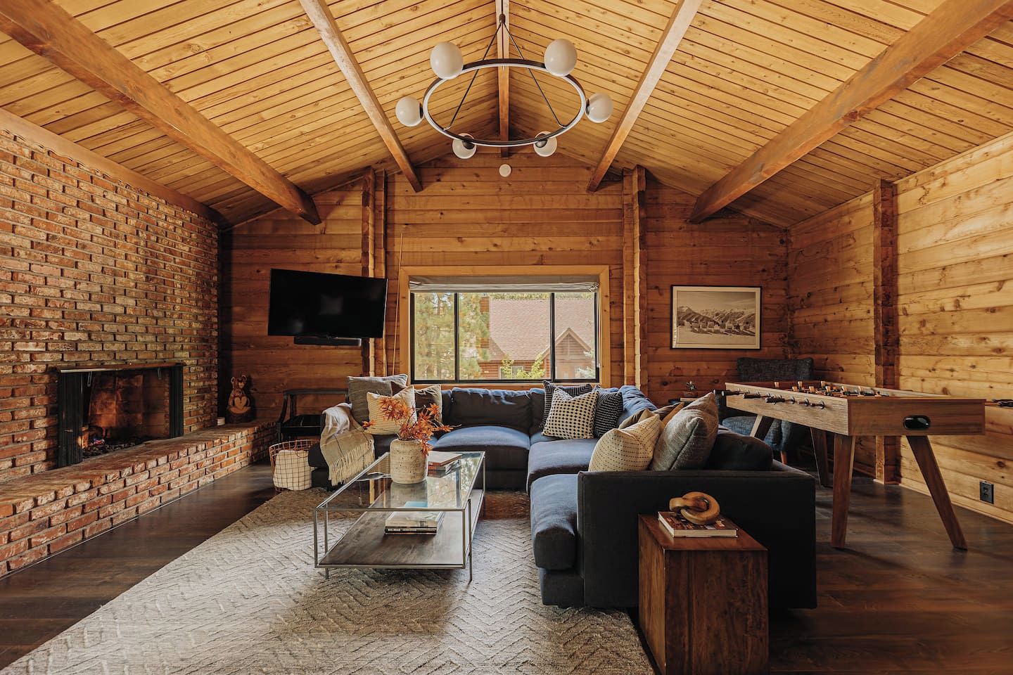 A cozy log cabin interior with a brick fireplace, a sofa set, a coffee table, and a foosball table.