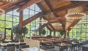 Un restaurante espacioso con techos altos, ventanas amplias y vigas de madera. Mesas y sillas dispuestas para comer.