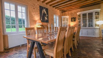 Un espace repas doté d’un sol en pierre, de chaises en bois, d’une table en verre et d’un buffet blanc aux portes en verre.
