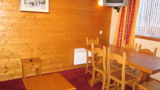 A wooden-paneled room with a dining table, chairs, a small table, and a television mounted on the wall. - Apartment in Plagne Village Near Ski Slopes (La Plagne-Tarentaise)