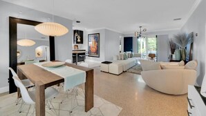 Uma sala de estar moderna com área de jantar, conjunto de sofás e iluminação pendente.