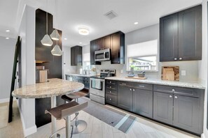 A modern kitchen with dark cabinets, a granite countertop, a built-in microwave, and a large window. - Modern Zen Retreat near Fort Lauderdale Beach (Oakland Park)