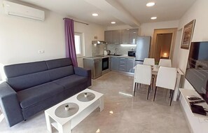 Ein modernes Wohnzimmer mit einem dunklen Sofa, einem weißen Couchtisch und einem Essbereich mit weißen Stühlen.