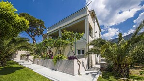 A modern two-story house with a covered patio, surrounded by lush greenery and palm trees. - Cozy home in Podstrana with private swimming pool, can be inside or outside (Podstrana)