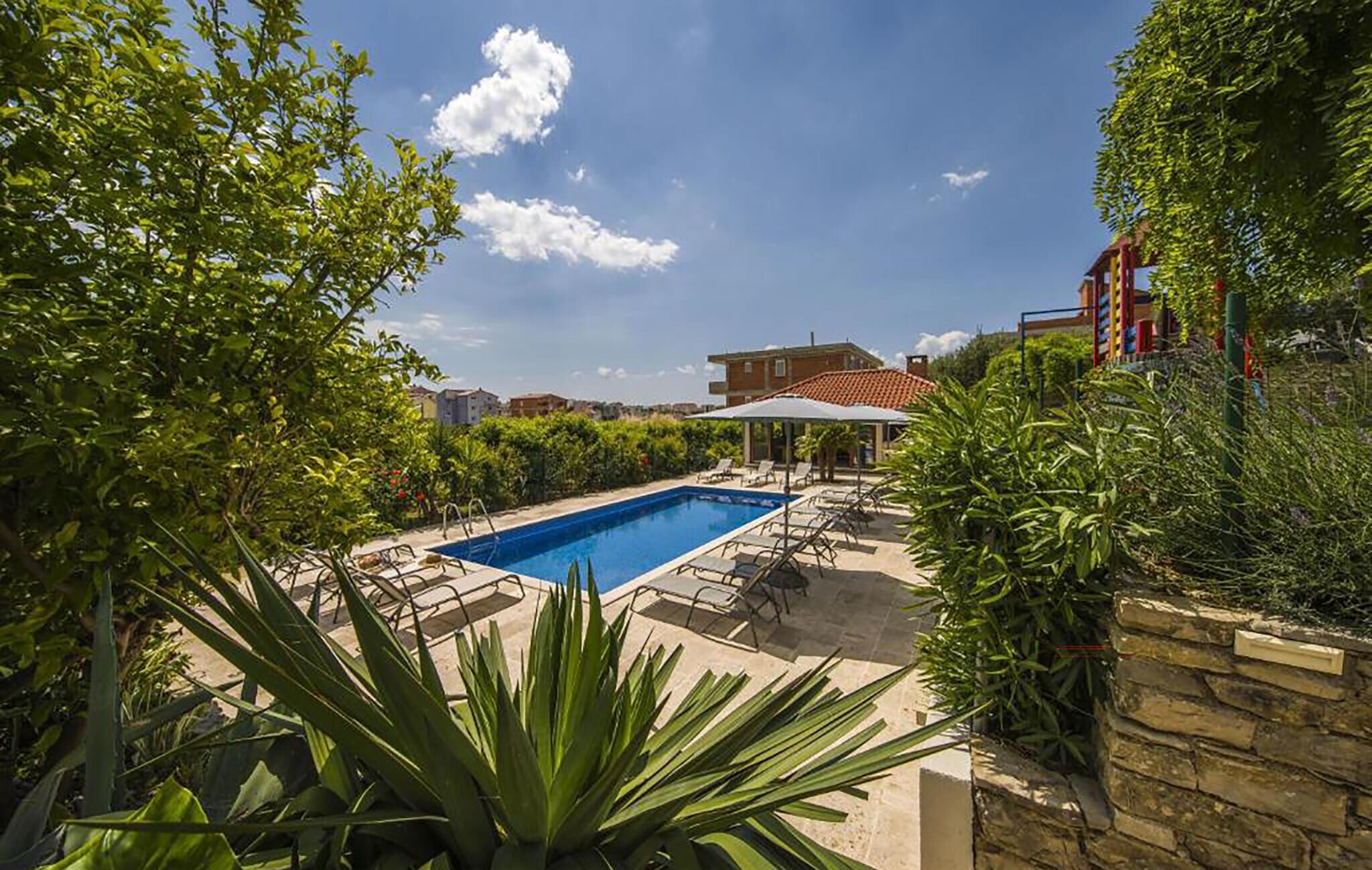 A swimming pool with lounge chairs, surrounded by greenery and a stone wall.