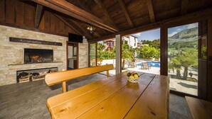 A wooden bench with a basket of fruit, a stone fireplace, and a view of a pool and greenery outside. - Cozy home in Podstrana with private swimming pool, can be inside or outside (Podstrana)