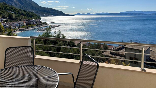 A balcony with a table and chairs overlooking a lake with a town and mountains in the background. - Amazing apartment in Podgora with house sea view (Podgora)