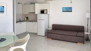A compact kitchen with white cabinets, a microwave, and a refrigerator. There's a brown sofa and a small table with chairs. - Amazing apartment in Podgora with house sea view (Podgora)