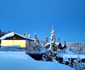 Un paysage enneigé avec une cabane aux parois vitrées et une maison en bois.