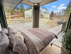 Une chambre avec un grand lit, une vue sur l’extérieur et une fenêtre avec des rideaux.