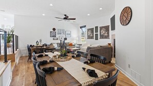 A spacious living room with a dining area, a ceiling fan, and a clock on the wall. - Private Pool & Pickleball Court | Pet-Friendly (Branson)