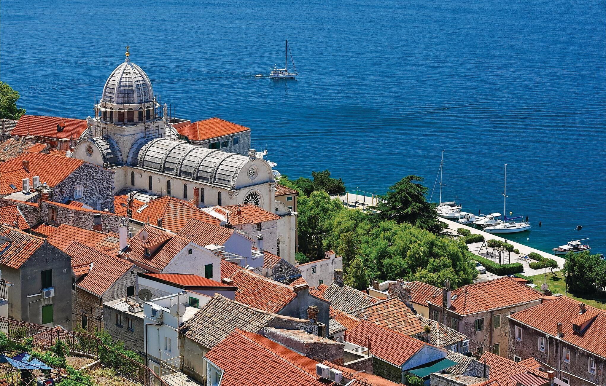 A coastal town with historic architecture, including a prominent church with a dome, and a marina with boats.