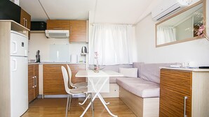 A compact kitchenette with a microwave, stove, and refrigerator. There is a dining table with chairs and a sofa. - Beautiful (sta)caravan in Drnis with WiFi (Drnis)