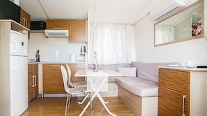 A compact kitchenette with a microwave, stove, and refrigerator. There is a dining table with chairs and a sofa. - Gorgeous (sta)caravan in Drnis with WiFi (Drnis)